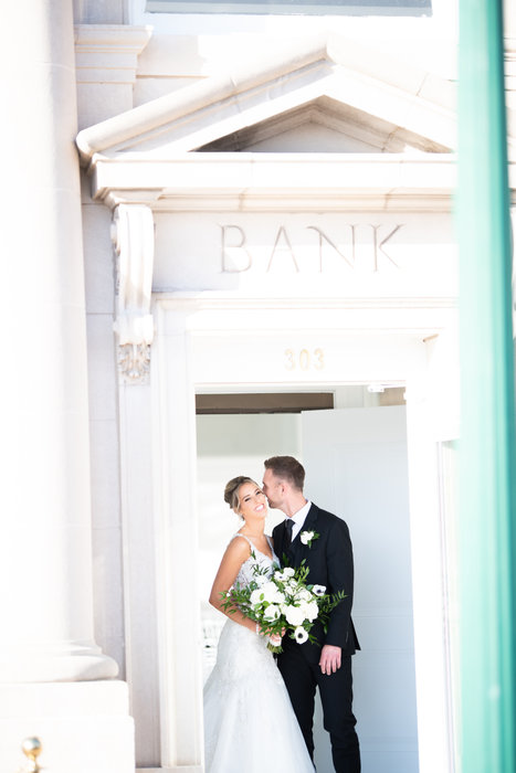 Ashley and Zach sharing a kiss in the doorway of a bank building.