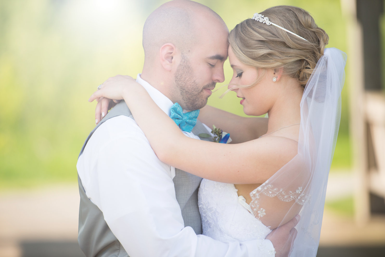 A bride and groom touching foreheads in soft green light.