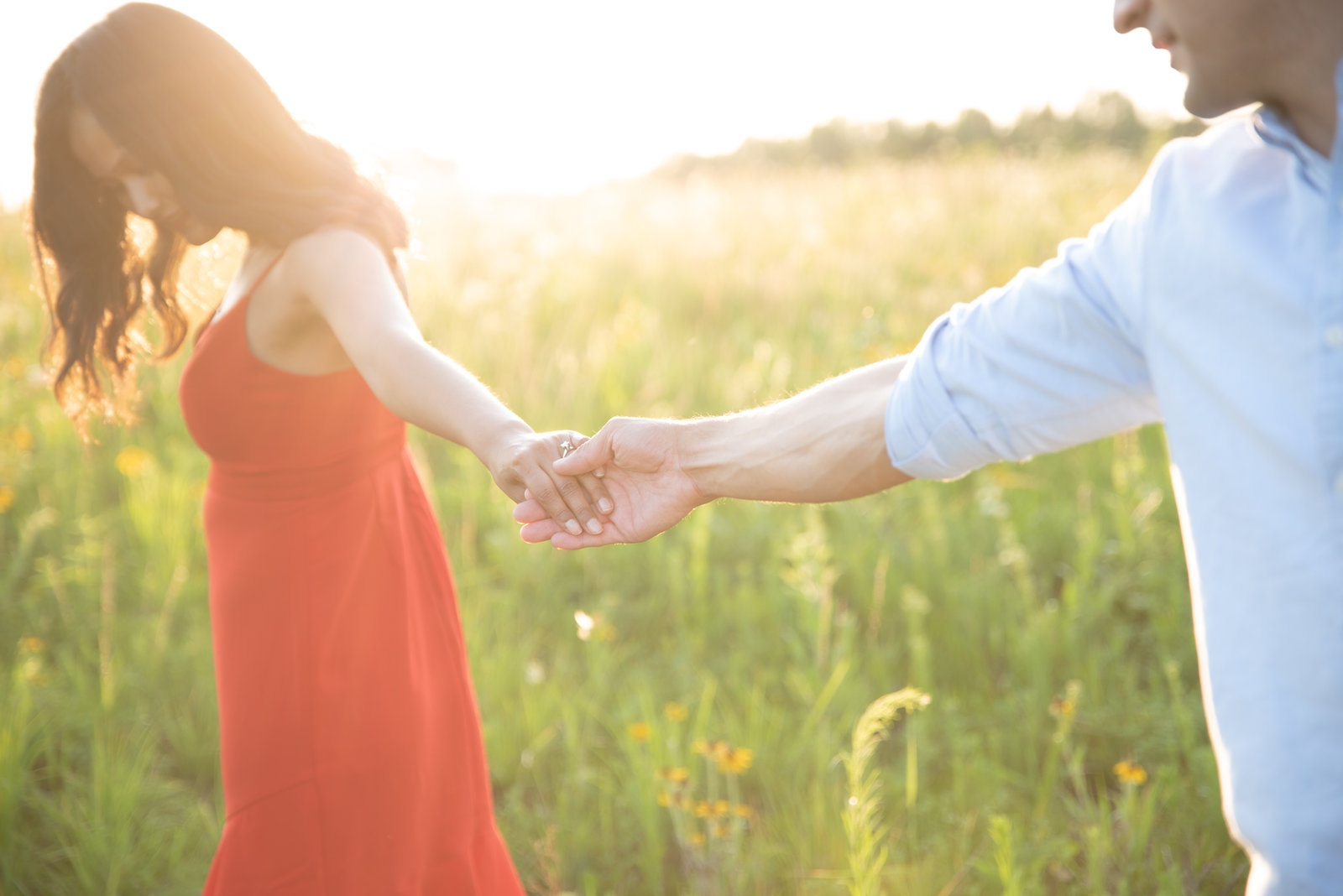 A woman in a red dress holding her partner's hand in a sunlit field.